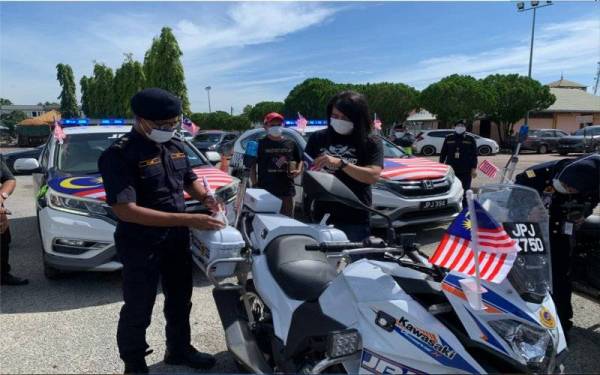 Hanif (kiri) bersama Eddie memasang bendera di sebuah motosikal milik JPJ di sini pada Khamis.