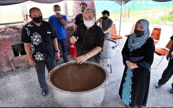 Suaibah memerhati Pengerusi Primula Beach Hotel, Datuk Mustafa Ali (tengah) mengacau bubur Asyura bersempena program kacau bubur Asyura dalam normal baharu, pada Khamis.