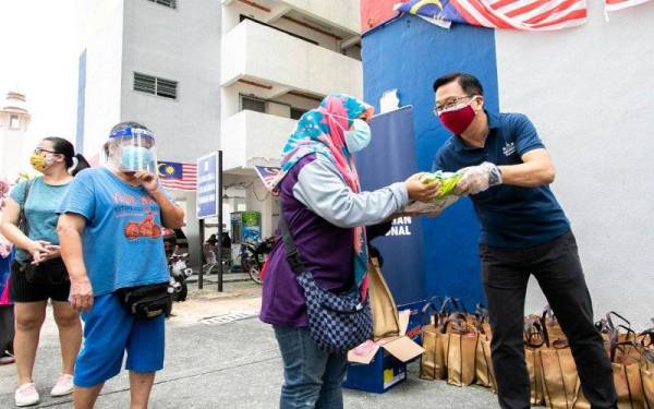 Dominic (kanan) mengedarkan barangan keperluan asas kepada penduduk di PPR Sri Wahyu, Jalan Ipoh di Kuala Lumpur pada Khamis.