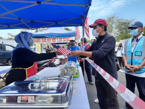 Hamdan menyerahkan Jalur Gemilang kepada peniaga dan penjaja di Tapak Niaga Sungai Isap, Kuantan pada Sabtu.