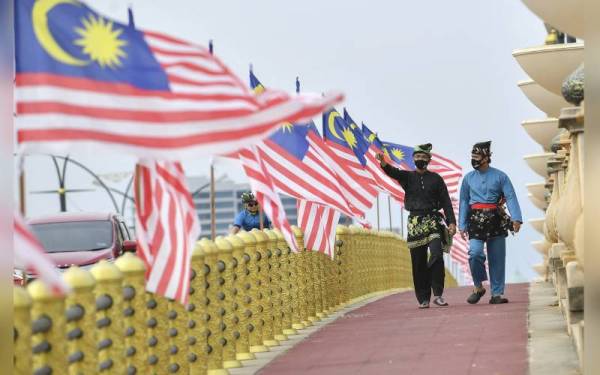 Dua ahli silat Mohd Khairul Kamaruzaman (kiri) dan Izwan Khuzzairie Azhar Ahmad berbaju Melayu lengkap bersampin dan bertanjak umpama pendekar zaman dahulu, menyusuri Jalur Gemilang yang berkibar megah di sepanjang Jambatan Seri Gemilang bagi menzahirkan rasa cintakan negara sempena sambutan Hari Kebangsaan ke-64. - Foto Bernama