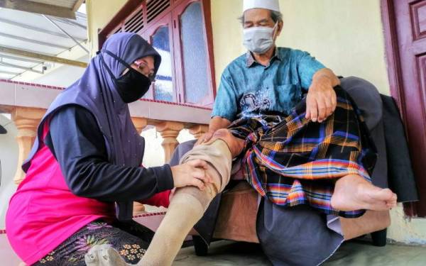 Yaacob dibantu anak sulungnya, Fadhilah Yaacob, 51, semasa memakai kaki palsu ketika ditemui di kediamannya di Kampung Bukit Kecik, Melor, Kota Bharu hari ini. 