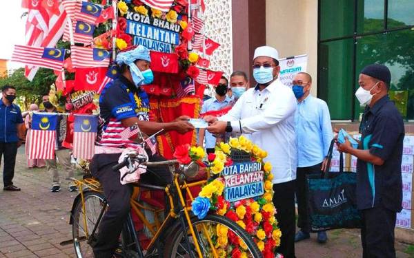 Ahmad Marzuk (dua dari kanan) sampaikan sumbangan kepada pengayuh beca pada Program Musaadah Yadim-Bank Islam kepada pengayuh beca di Dataran Muhammadi, Kota Bharu pada Sabtu.