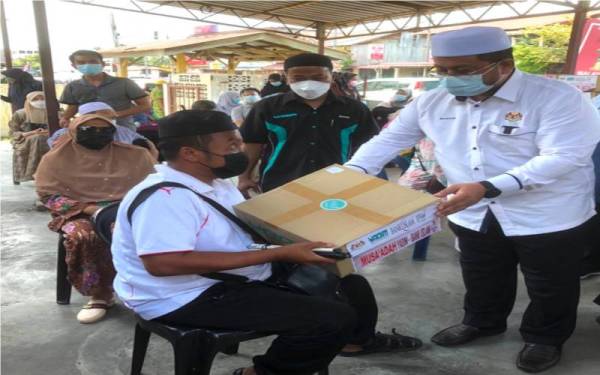 Ahmad Marzuk (kanan) menyampaikan sumbangan kotak makanan dan wang tunai kepada salah seorang penerima di Pejabat Pertis Kelantan di Beris Kubur Besar, pada Sabtu.