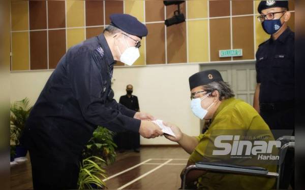 Mazlan (kiri) menyampaikan sumbangan kepada warga kerja dan pesara PDRM yang terlibat bencana banjir lumpur di Gunung Jerai, Yan pada Ahad.