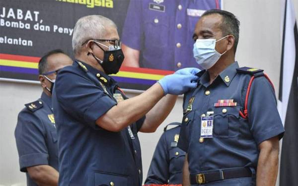 Mohammad Hamdan (kiri) menyampaikan tanda pangkat kepada Pegawai Bomba Tinggi II, Bazri Abdul Rahman pada lawatan kerja ke JBPM Kelantan pada Ahad.