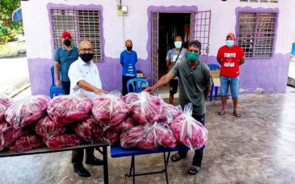 Nor Azmi (kiri) menyerahkan sumbangan ikan kembung kepada wakil penduduk orang asli di Paya Mengkuang, Temerloh pada Selasa.