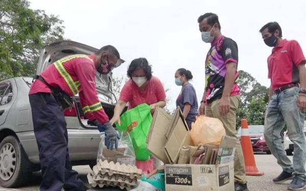 Sharudin (dua,kanan) membantu seorang pengunjung yang menghantar barangan kitar semula di BBC Taman Gelora pada Sabtu.