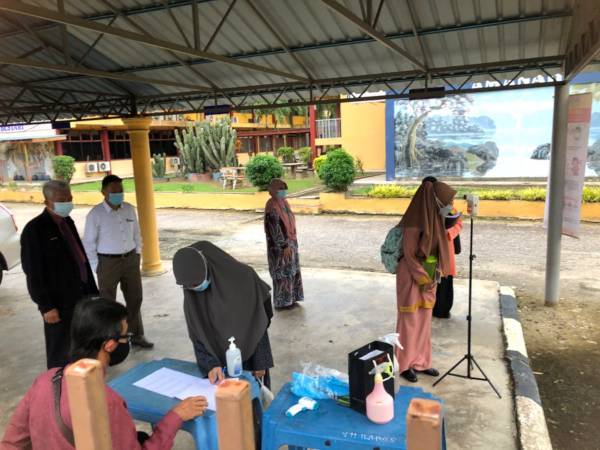 Pelajar-pelajar melakukan saringan suhu badan dan merekodkan kehadiran di pintu masuk sekolah dengan pemantauan para guru. Foto SINAR HARIAN