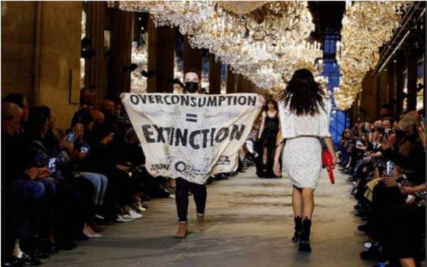 Seorang aktivis membawa sepanduk yang tertera "Overconsumption = Extinction" di pertunjukan fesyen Louis Vuitton pada Selasa. - Foto Reuters