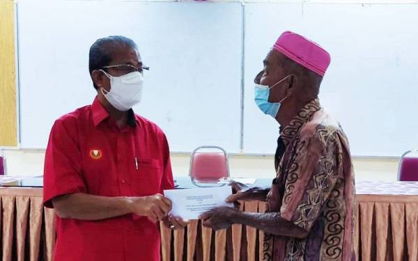 Ku Abdul Rahman (kiri) menyerahkan Sumbangan Wang Ihsan Kumpulan Wang Amanah Bantuan Bencana Negara Mangsa Kejadian Aliran Puing Daerah Yan Fasa Pertama kepada seorang mangsa banjir di Dewan Masjid Jamek Badlishah, Yan pada Khamis.