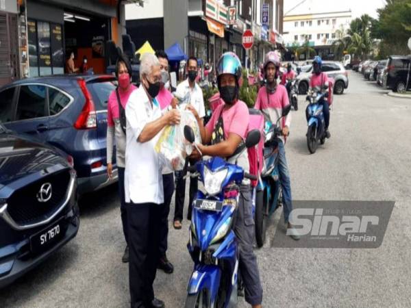 Hassan (kiri) menyampaikan bakul makanan kepada penunggang p-hailing Foodfanda Di Pejabat Pusat Khidmat Parlimen Pasir Gudang, Kota Puteri, Pasir Gudang pada Sabtu.