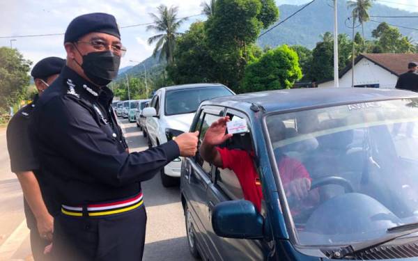 Shafien (kiri) memeriksa kad vaksinasi seorang pemandu kereta yang merentas negeri dari Terengganu di SJR Bukit Yong, Pasir Puteh pada Isnin.