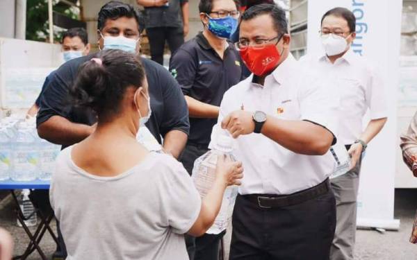 Amirudin (kanan) mengagihkan botol air minuman kepada penduduk di Pangsapuri PKNS Seksyen 17, Petaling Jaya pada Khamis.