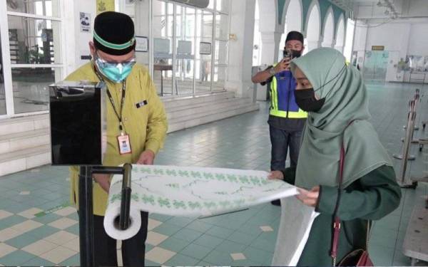 Badli Shah (kiri) membantu salah seorang jemaah musafir menggunakan sejadah pakai buang.