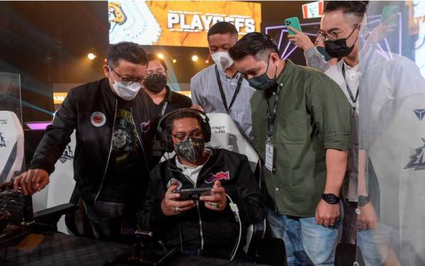 Ahmad Faizal (duduk) sedang mencuba permainan e-sukan sambil diperhatikan oleh Timbala Menteri Belia dan Sukan Senator Datuk Seri Ti Lian Ker (kiri) pada Majlis Penutup Mobile Legends Pro League (MPL) Malaysia Season 8 di Tropicana Gardens Mall, pada Ahad.  Turut sama Naib Presiden Hal Ehwal Awam dan Kerajaan IOESports Joel Goh.  - Foto Bernama 