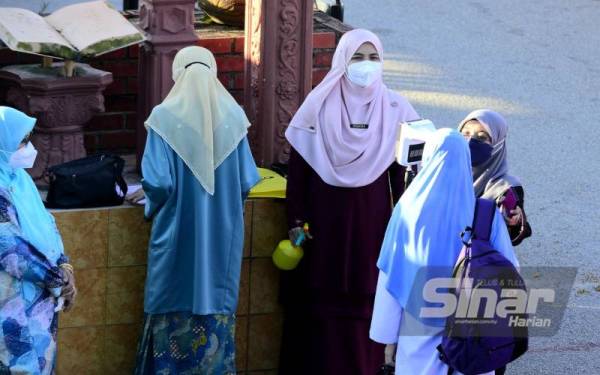 Guru SMK Paya Besar berada di pintu pagar sekolah bagi memastikan pelajar mematuhi SOP ditetapkan sebelum memulakan sesi persekolahan secara bersemuka pada Isnin.