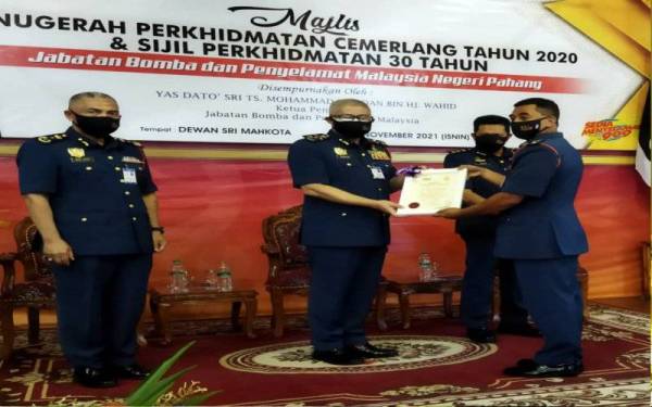 Mohammad Hamdan menyampaikan sijil Anugerah Perkhidmatan Cemerlang kepada Penolong Pengarah Bahagian Operasi JBPM Pahang, Ismail Abdul Ghani yang mendahului barisan penerima di Ibu Pejabat JBPM Pahang, Indera Mahkota, Kuantan pada Isnin.