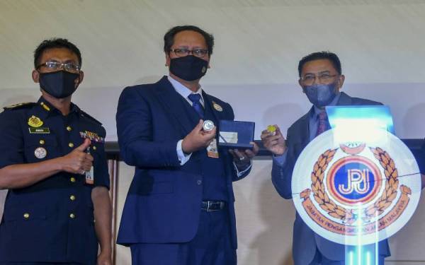 Zailani (tengah) dan Penolong Gabenor Bank Negara Abu Hassan Alshari Yahya (kanan) menunjukkan duit syiling kenangan ulang tahun ke-75 JPJ selepas melancarkannya hari ini. Foto Bernama