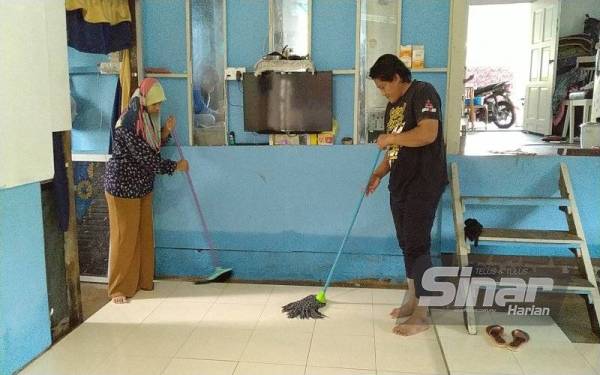 Raja Yusuf Shah bersama isterinya, Siti Nurul Aini Mohd Salim, 35, mengeringkan lantai rumah mereka yang dinaiki air pada awal pagi Jumaat.