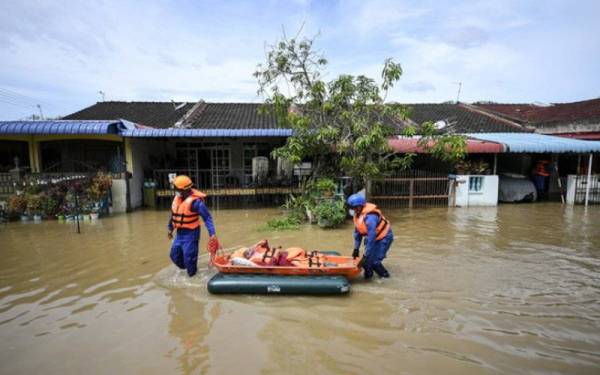 Anggota APM Kedah membantu seorang warga emas, Supiah Musa, 70, yang menghadapi masalah kesihatan untuk dipindahkan ke kediaman pembantu rumahnya, P Devika, 57, selepas kawasan kediamannya dinaiki air. - Foto Bernama