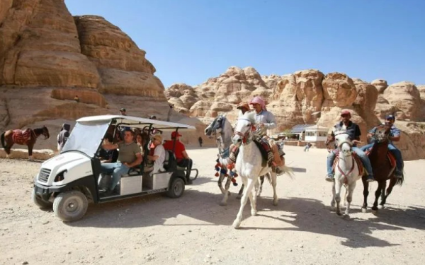 Beberapa lelaki menunggang kuda manakala para pelancong menaiki kereta bugi elektrik di bandar purba Petra, Jordan baru-baru ini.