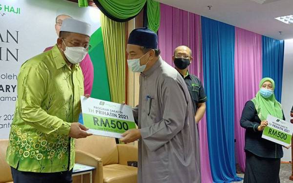 Ahmad Marzuk (kiri) menyampaikan zakat kepada peniaga kecil ketika Program Tabung Haji (TH) Prihatin di Kota Bharu pada Sabtu.