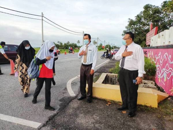 Mahayadin (dua dari kanan) bersama Ketua Guru Disiplin, Mohd Shukor Salleh menyambut kedatangan pelajar di pintu pagar utama sekolah.