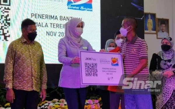 Rina (dua dari kiri) menerahkan replika kad bantuan kewangan tanpa tunai kepada seorang penerima pada Majlis Pelancaran Peluasan Program Bayaran Bantuan Tanpa Tunai dengan kerjasama Bank Islam Malaysia Berhad (BIMB) di Taman Sinar Harapan pada Isnin.