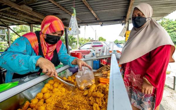 Rakiah Mamat, 50, (kiri) melayan pelanggannya Marzukiah Yaacob, 56, yang membeli ubi getuk di gerainya di Kampung Jambu Merah Melor di sini. - Foto Bernama