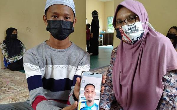 Anak dan ibu arwah menunjukkan gambar kenangan Muhamad Ridhwan yang lemas akibat bot dinaiki terbalik pada kedudukan 5.5 batu nautika barat daya jeti Tanjung Dawai pada Selasa.