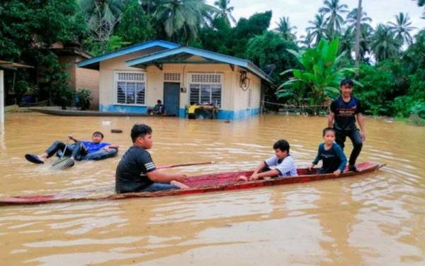 Kanak-kanak dan remaja menggunakan perahu kayu untuk bermain air akibat banjir yang melanda di halaman rumah mereka ketika tinjauan di Kampung Manek Urai Lama pada Sabtu. - Foto Bernama