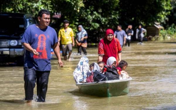 Penduduk, Khairul Anuar Muhamad, 37, (kiri) menarik sampan bersama isteri dan anaknya untuk berpindah ke rumah saudara mereka setelah rumah mereka ditenggelami banjir ketika tinjauan di Kampung Tersang Rantau Panjang pada Isnin. - Foto Bernama