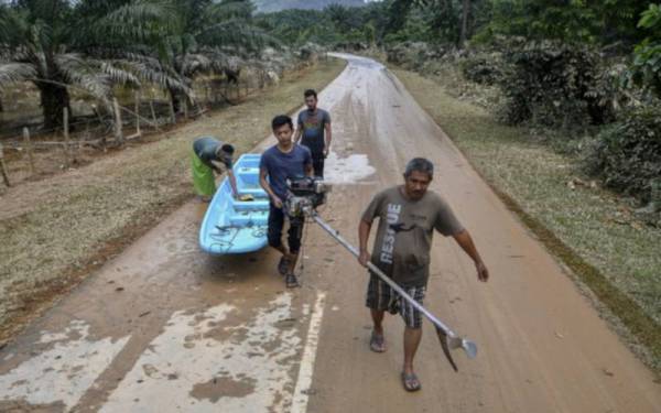 Penduduk Kampung Kuala Nal bergotong royong mengangkat sebahagian bot yang tersadai di atas jalan yang digunakan bagi mengangkut penduduk yang terjejas akibat banjir ketika tinjauan Bernama pada Selasa. - Foto Bernama