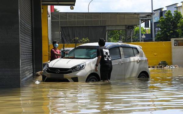 Penduduk setempat membersihkan kereta yang masih ditenggelami banjir di Taman Seri Muda Seksyen 25. -Foto Bernama