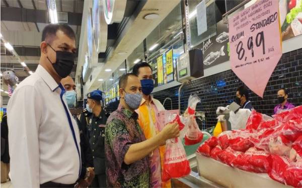 Mohd Nurkhuzaini (tengah) melihat ayam yang dijual di Mydin Hypermarket Gong Badak, di Kuala Nerus pada Khamis.