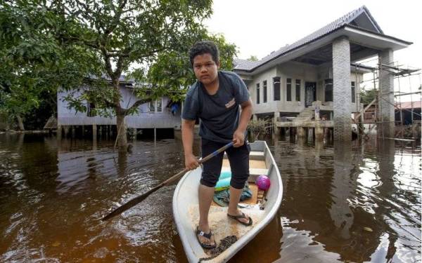 Penduduk setempat, Adam Faiz Izham Musa,14, kembali ke rumahnya setelah keadaan banjir semakin pulih ketika tinjauan di Kampung Terusan pada Isnin. - Foto Bernama