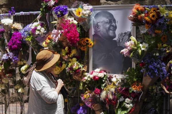 A woman looks at an image and floral tributes for the late Archbishop Desmond Tutu, at St George's Cathedral, Cape Town, South Africa, Dec 28, 2021. There is a seven day send-off including a state funeral, lying in state and church service at the St. George's Cathedral for the anti-apartheid activist and Nobel Peace Price laureate who died on Dec 26, 2021 at the age of 90. (Source: EPA/NIC BOTHMA)