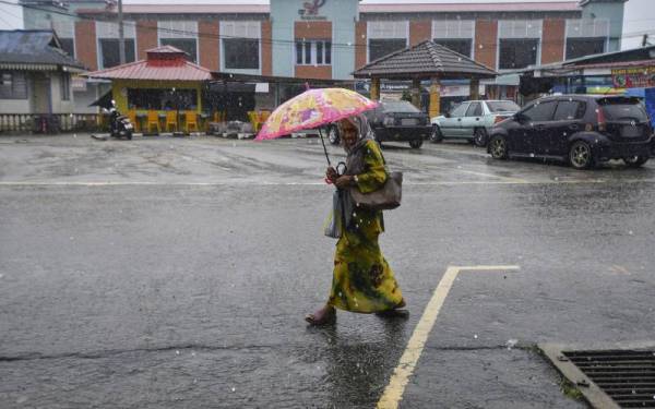 Seorang wanita berpayung meredah hujan ketika melakukan aktiviti harian semasa hujan ketika tinjauan di Rantau Panjang hari ini. - Foto Bernama