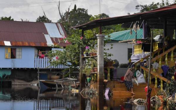 Penduduk, Rohani Abdul Karim menyiang ikan di tangga rumahnya yang masih digenangi air pada Rabu. - Foto Bernama