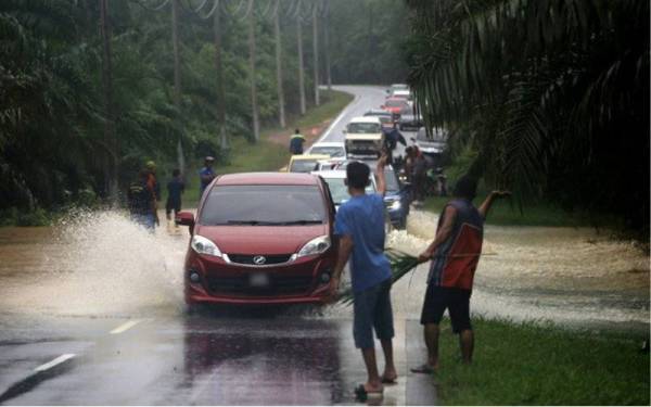 Penduduk kampung mengambil insiatif mengawal lalu lintas di laluan Jalan Jelai-Gemas Tambahan yang turut tenggelam akibat dinaiki air pada Ahad. - Foto Bernama