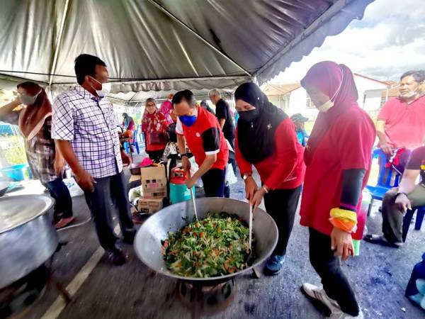 Ahmad (tiga dari kanan) membantu menggoreng sayur ketika melawat Taman Pinggiran Felda Sungai Kelamah yang terjejas akibat banjir. Turut kelihatan Ahli Dewan Undangan Negeri Gemencheh, Datuk Mohd Isam Mohd(kiri).