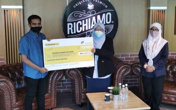 Pengarah Pemasaran Richiamo Coffee, Adam Kassim (kiri) menyerahkan replika cek Tabung Cakna OKU UiTM kepada Dr Roziah sempena pembukaan cawangan ke-70 di Bangunan Canseleri Syed Sirajudin UiTM Shah Alam di sini pada Selasa.