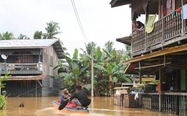 Sebuah keluarga menggunakan sampan untuk keluar selepas rumah mereka ditenggelami air di Kampung Tolungan, Pamol, Beluran pada Selasa. - Foto Bernama
