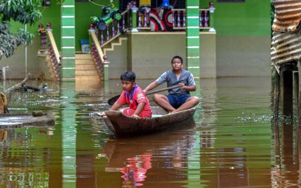 Nik Mohd Aniq Mohd Adnan, 14, (kanan) bersama rakan Mohd Abid Khalis Mohd Roslan, 7, (kiri) terpaksa mendayung sampan untuk keluar dari kawasan kediaman yang masih digenangi air sejak awal November lalu. - Foto Bernama 