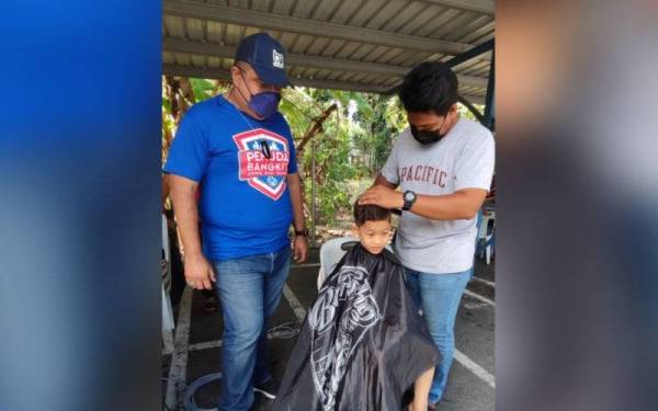 Syed Mohd Johan (kiri) melihat seorang kanak-kanak mendapatkan perkhidmatan gunting rambut percuma di di Masjid Al-Rahmah Taman Wira, di sini,pada Sabtu.