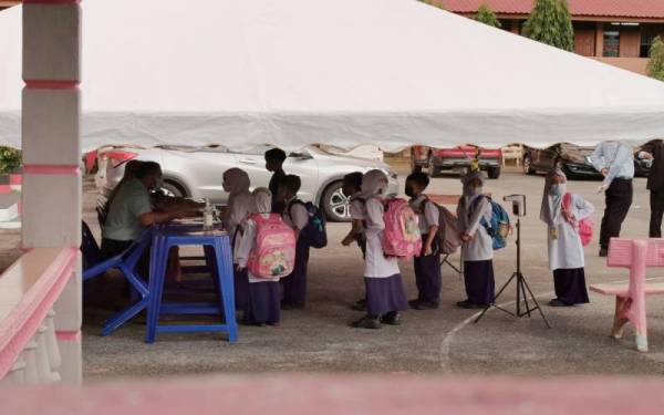 Sebahagian murid yang memulakan sesi persekolahan penggal tiga 2021/2022 di Sekolah Kebangsaan (SK) Ladang di Kuala Terengganu pada Ahad beratur untuk memeriksa suhu badan serta melakukan imbasan kod QR bagi kehadiran ke sekolah.