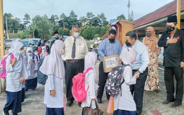 Rais (dua dari kanan) ketika mengedarkan pelitup muka kepada murid-murid di SK Tanjung Minyak pada Isnin.