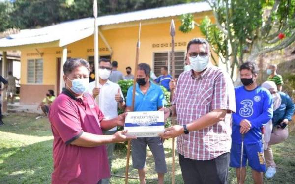 Mohd Syahbuddin (kanan) menyampaikan sumbangan kepada orang asli di Pos Bihai, Gua Musang.