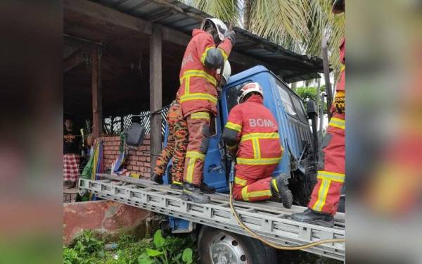 Anggota bomba berusaha mengeluarkan mangsa yang tersepit selepas treler dipandunya terbabas ke dalam parit dan melanggar tembok bengkel kereta di Jalan Kapar Batu 15 pada Khamis.